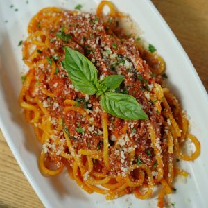Close-up of Italian spaghetti adorned with fresh basil and parmesan cheese served on a white plate.