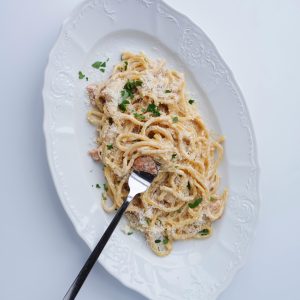 Close-up of spaghetti carbonara with cheese and herbs on a white plate, featuring a fork.