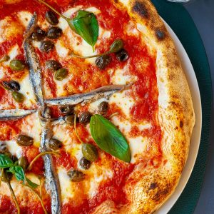 Delicious Neapolitan pizza topped with anchovies, olives, and basil, perfect for an Italian cuisine experience.