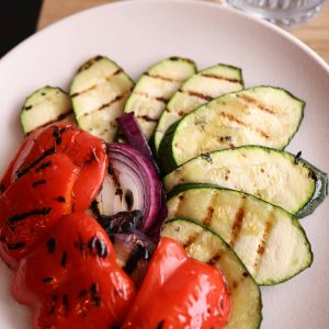 A plate of grilled vegetables including red bell pepper, zucchini, and red onion, perfect for a healthy meal.